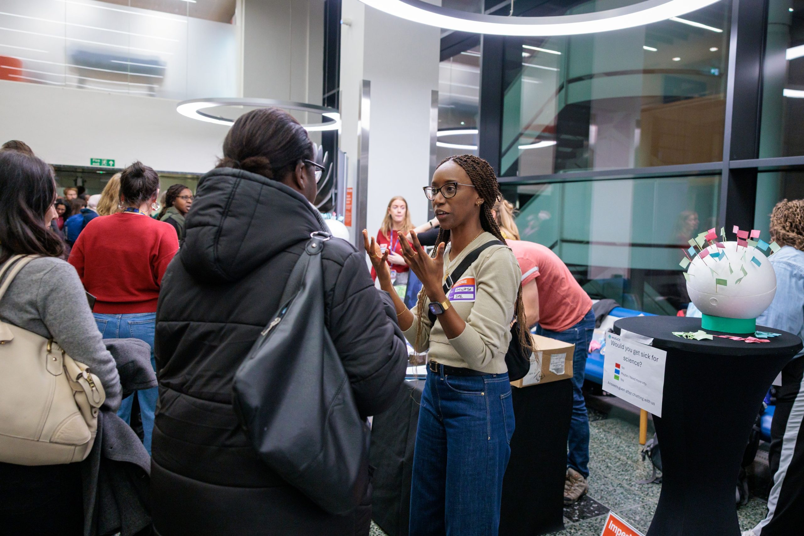 Photograph of MUSICC staff in conversation with members of the public at the Would You Get Sick for Science stand. One of the virus models can be seen in the background.