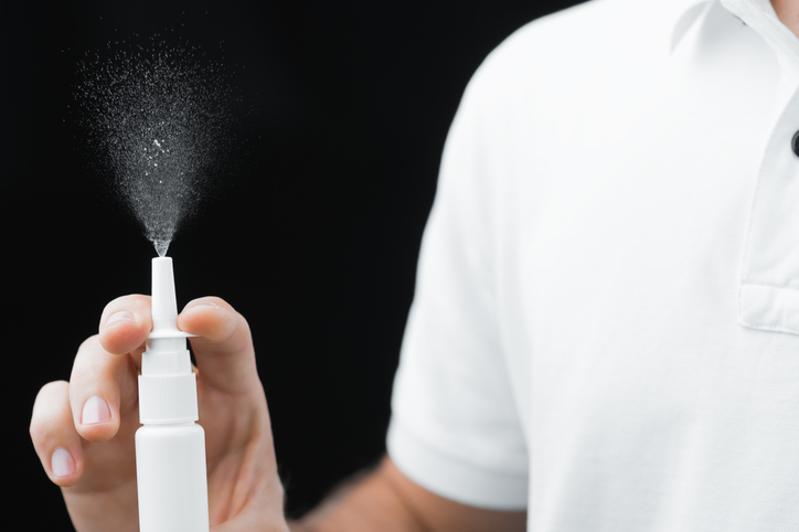 Photograph of a man in a white shirt on a black background checks the nasal spray.