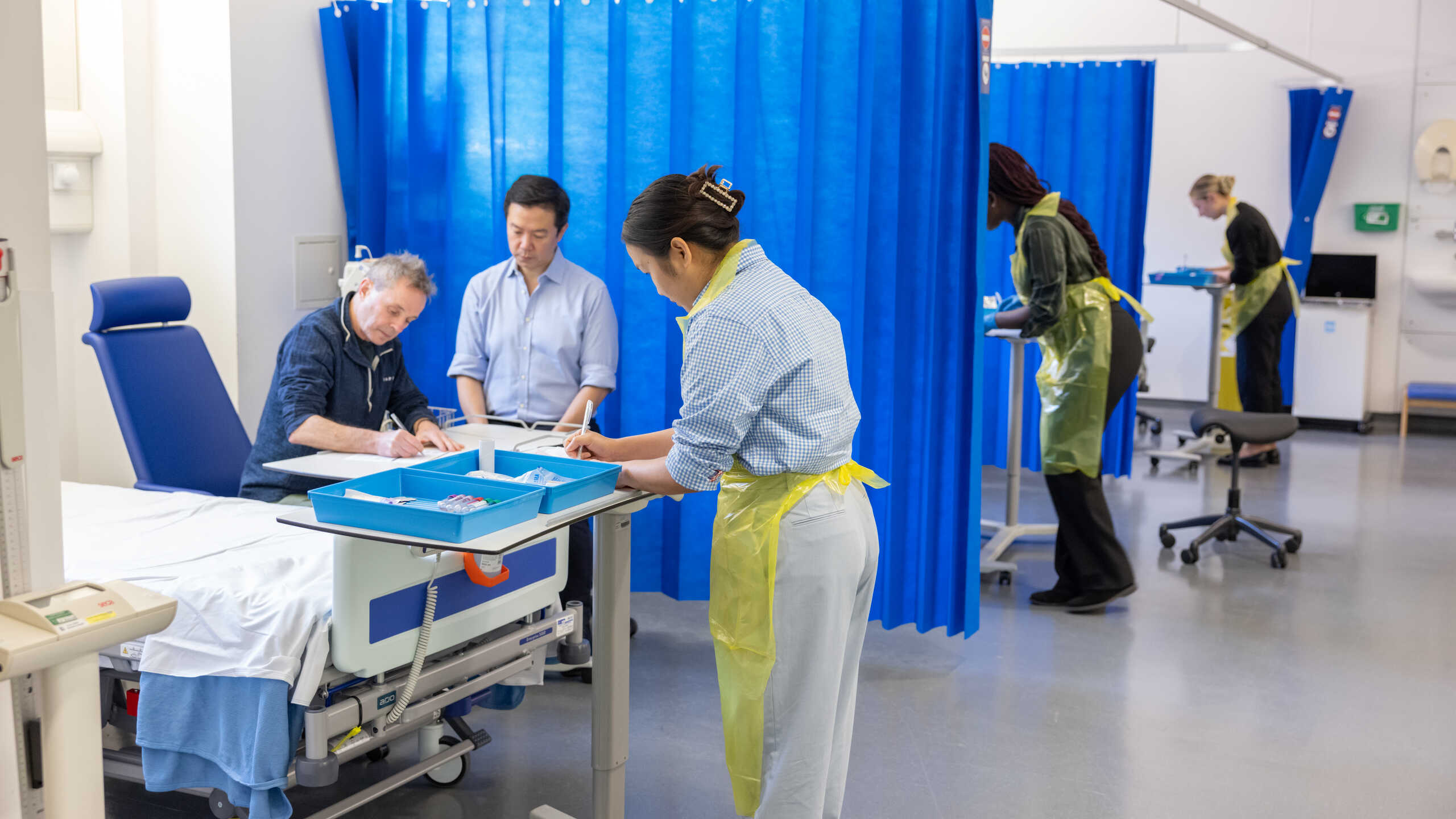 Photograph of a human challenge study. Multiple medical staff are monitoring patients and recording observations.