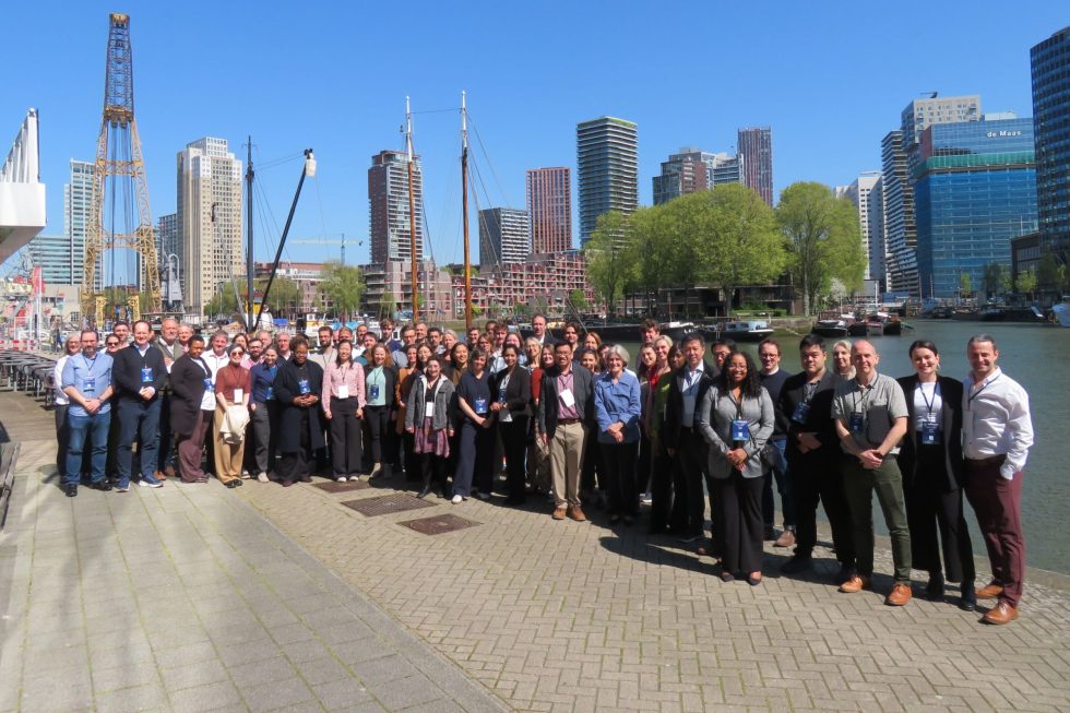 Photograph of the MUSICC consortium members stood on a dockside in front of the Rotterdam skyline on a sunny day.