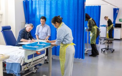 Photograph of a human challenge study. Multiple medical staff are monitoring patients and recording observations.