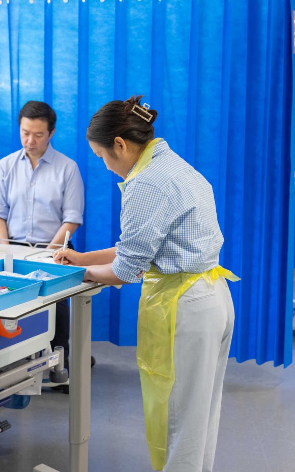 Photograph of a human challenge study. Multiple medical staff are monitoring patients and recording observations.